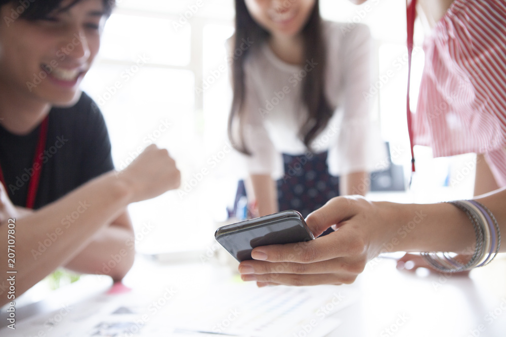 会議中にスマートフォンを見て楽しそうに話し合う三人