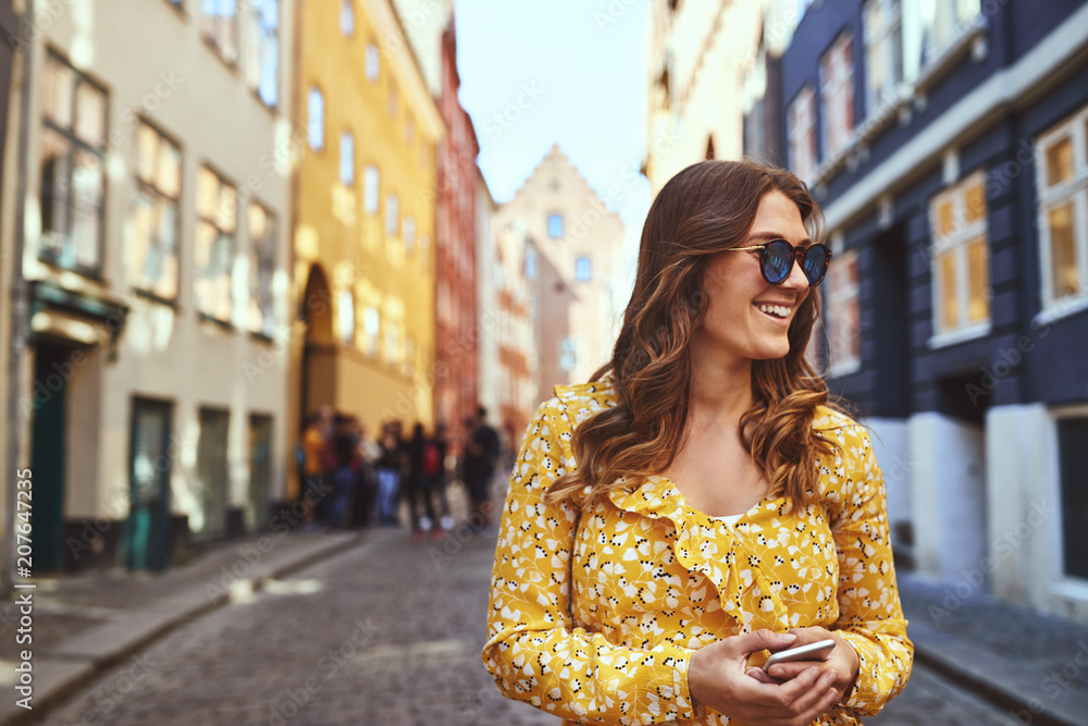 Smiling woman holding her cellphone while walking through the ci