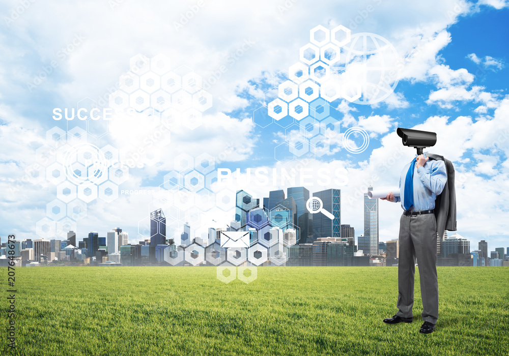 Camera headed man standing on green grass against modern cityscape