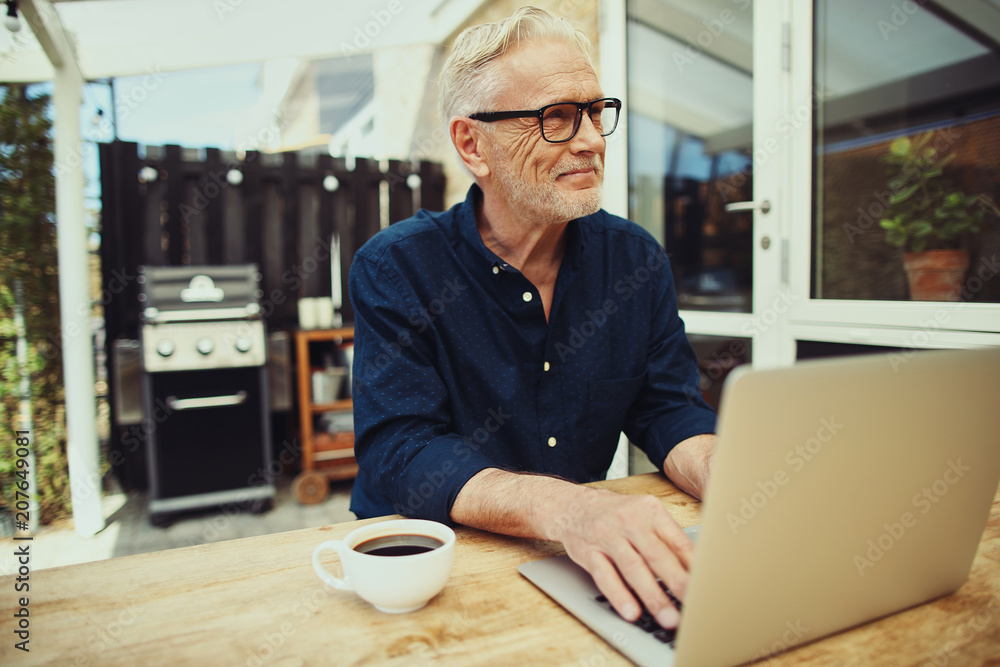 Smiling senior man working with a laptop on his patio