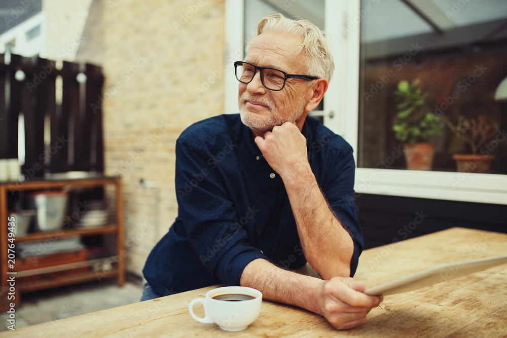 Content senior man sitting on his patio using a digital tablet