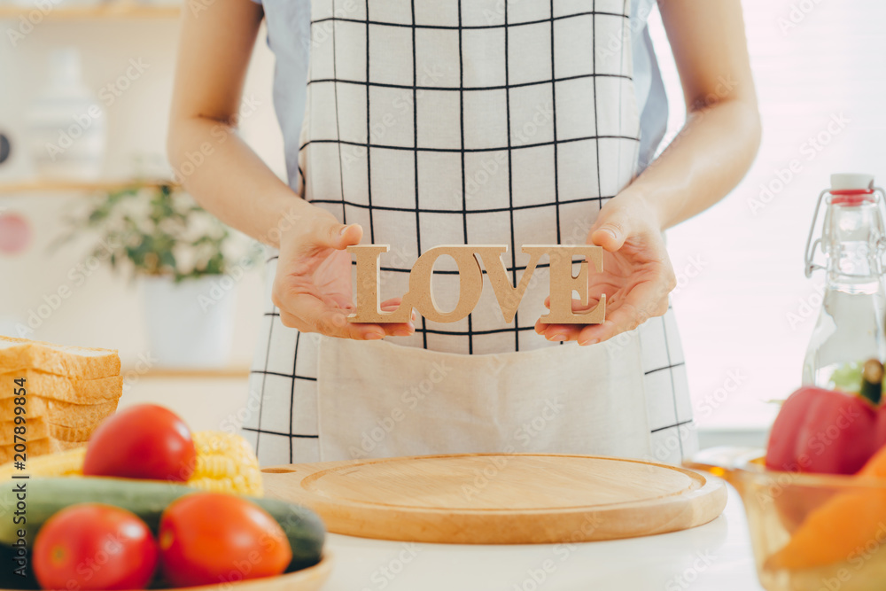 一个女人拿着木制字母LOVE在厨房做饭。