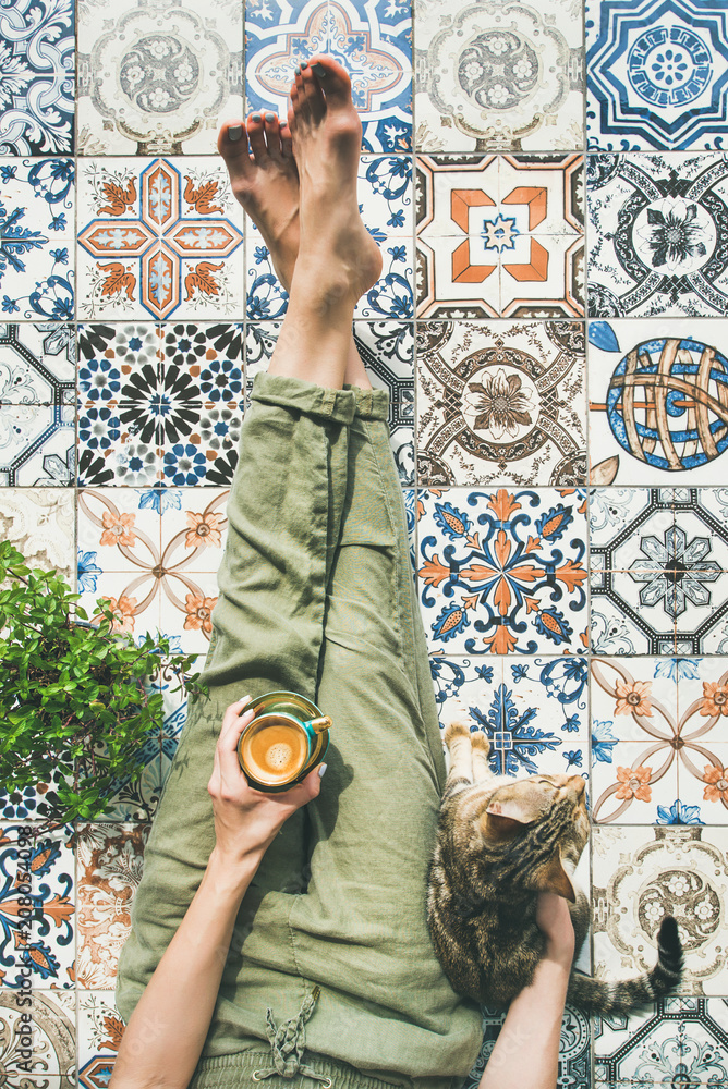 Lazy morning on terrace. Flat-lay of womans legs in cosy linen pants, plant, cat and cup of coffee i