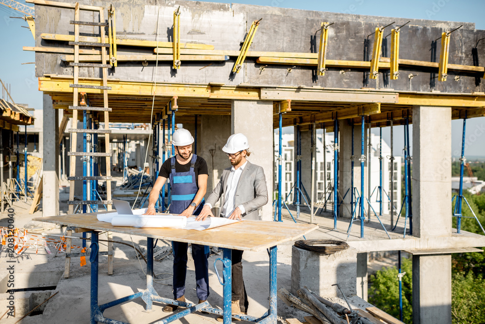 Engineer with worker in uniform working with architectural drawings at the table on the construction