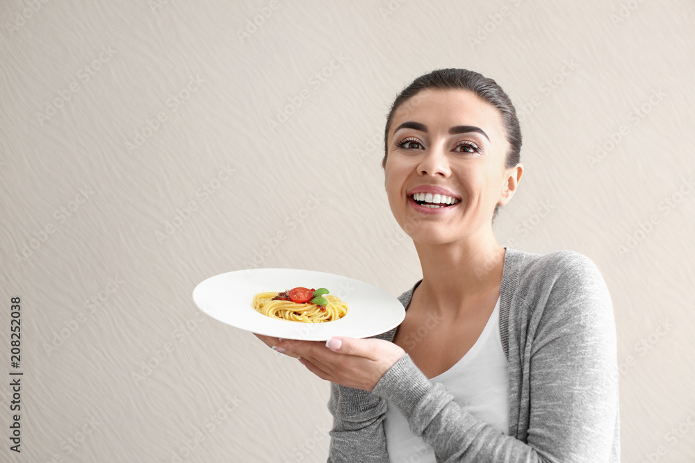 Young woman with plate of tasty pasta on light background