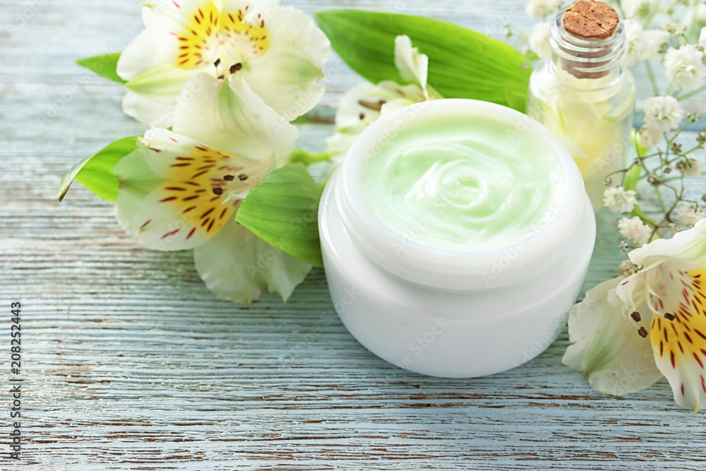 Jar of body cream and beautiful flowers on wooden background