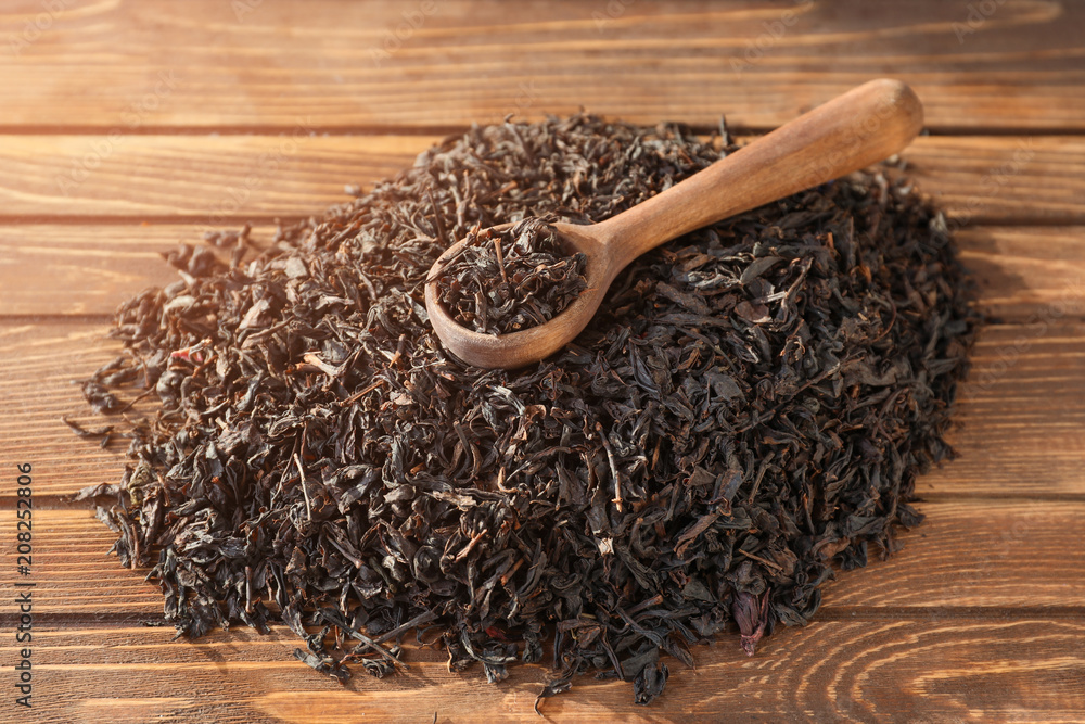 Spoon and heap of dry tea leaves on wooden background