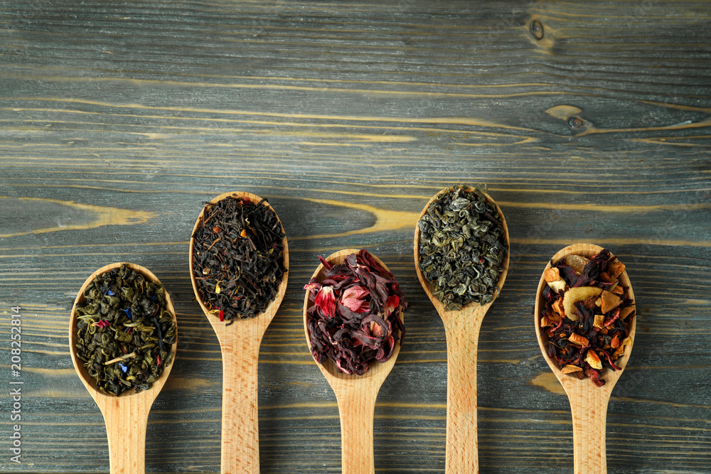 Variety of dry tea in spoons on wooden background