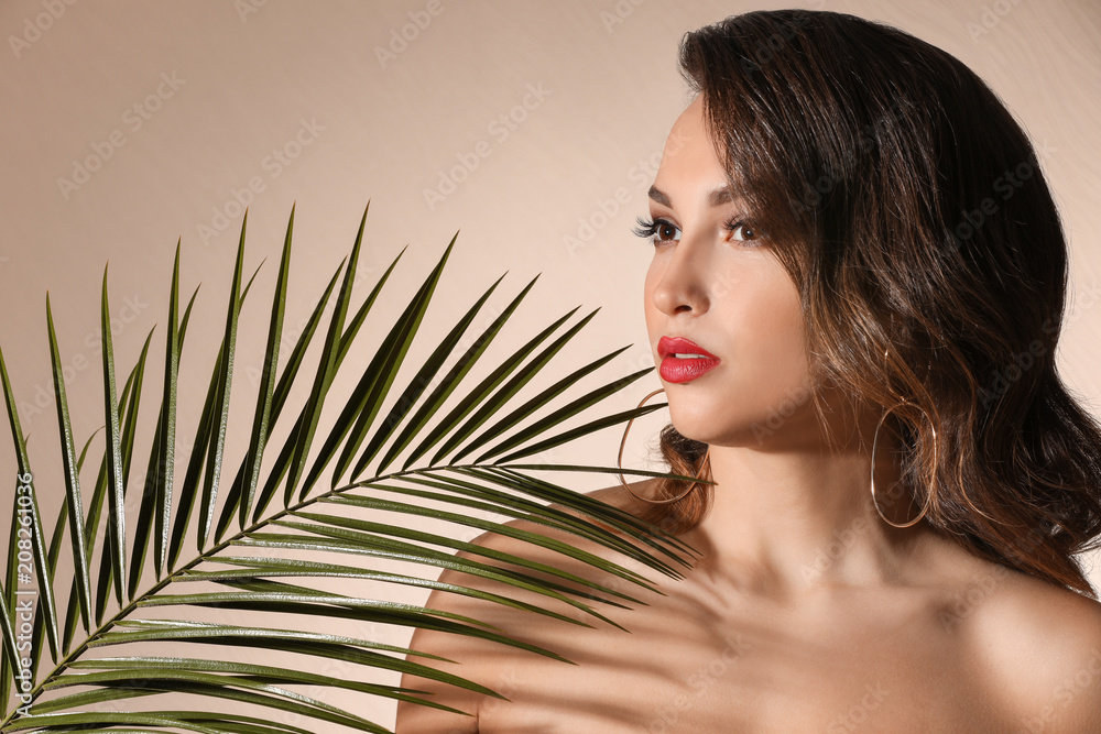 Portrait of young woman with beautiful professional makeup and palm leaf on light background