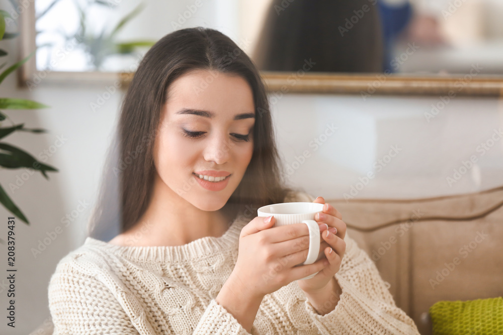 漂亮的年轻女人，家里有一杯热茶，透过窗户看