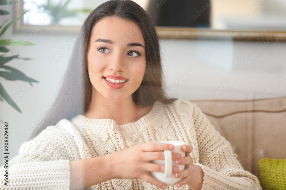 漂亮的年轻女人，家里有一杯热茶，透过窗户看