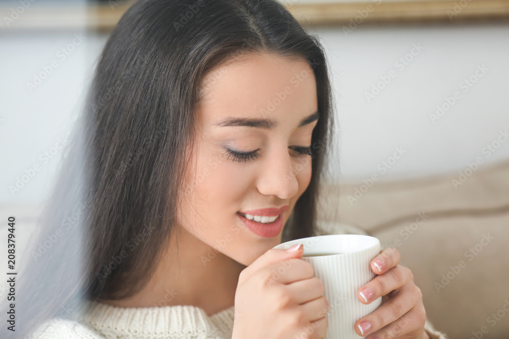 家里有一杯热茶的漂亮年轻女人，透过窗户看