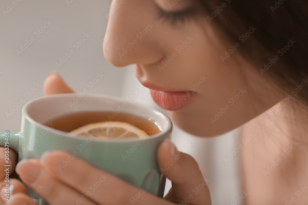 Beautiful young woman with cup of hot tea at home, closeup