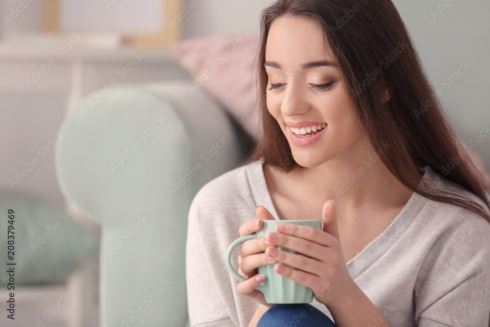 Beautiful young woman with cup of hot tea at home