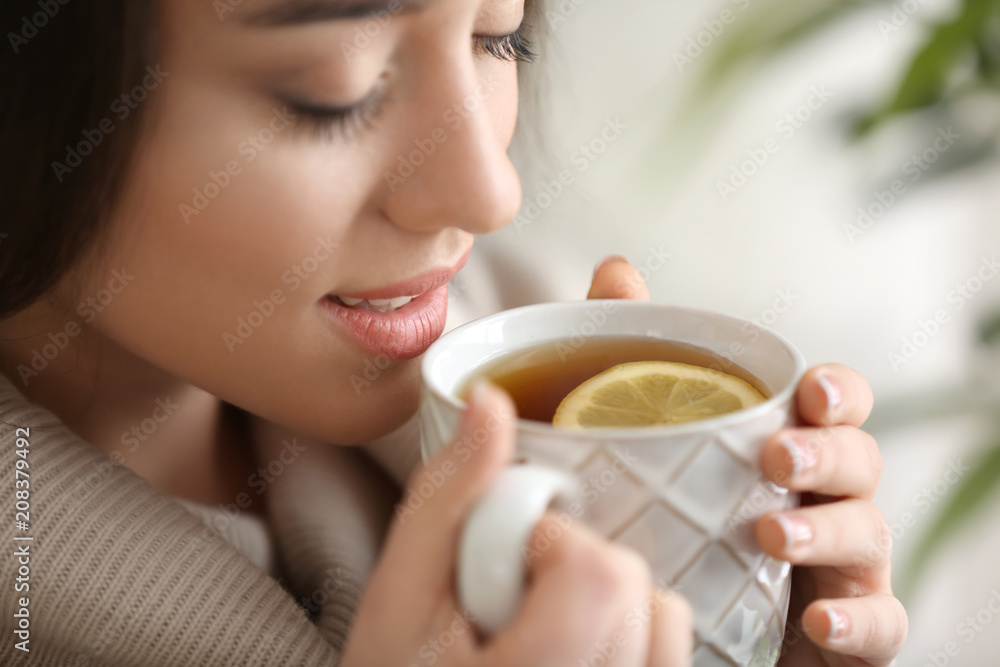 Beautiful young woman with cup of hot tea at home, closeup