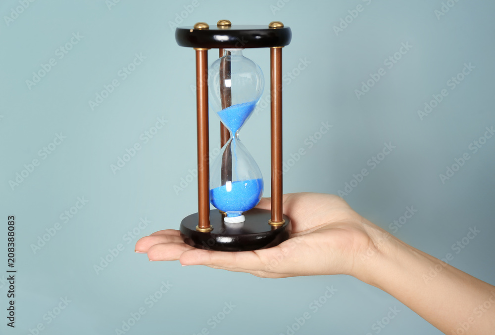 Woman holding hourglass on color background. Time management concept