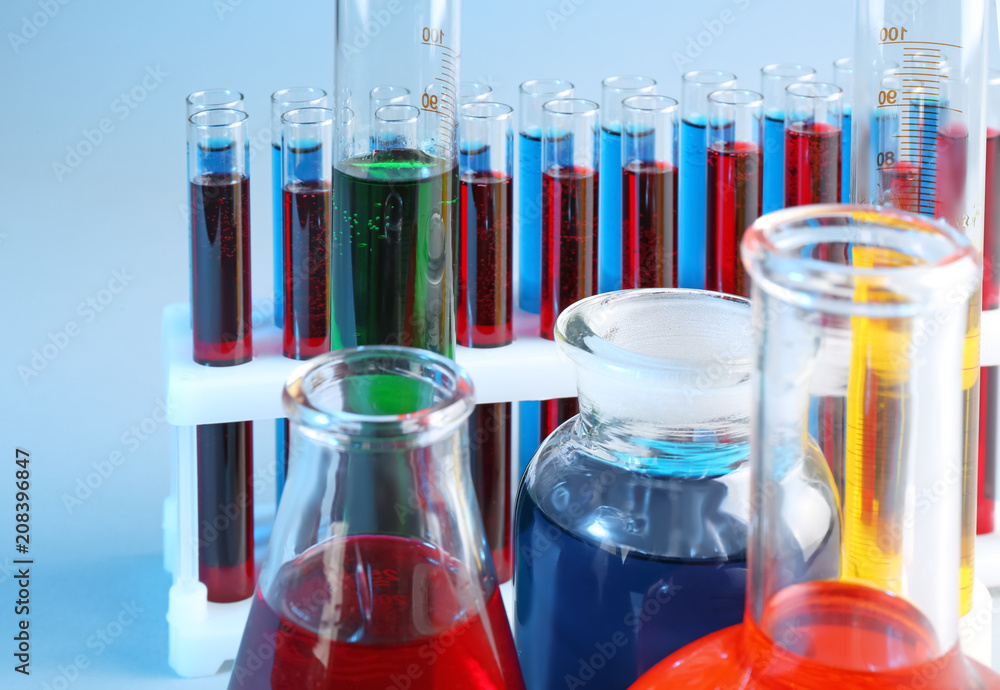 Chemical glassware with different liquids on color background