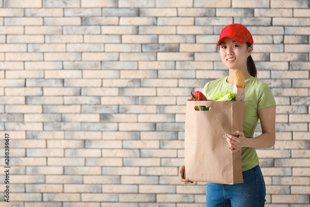 Asian woman with products in paper bag on brick wall background. Food delivery service