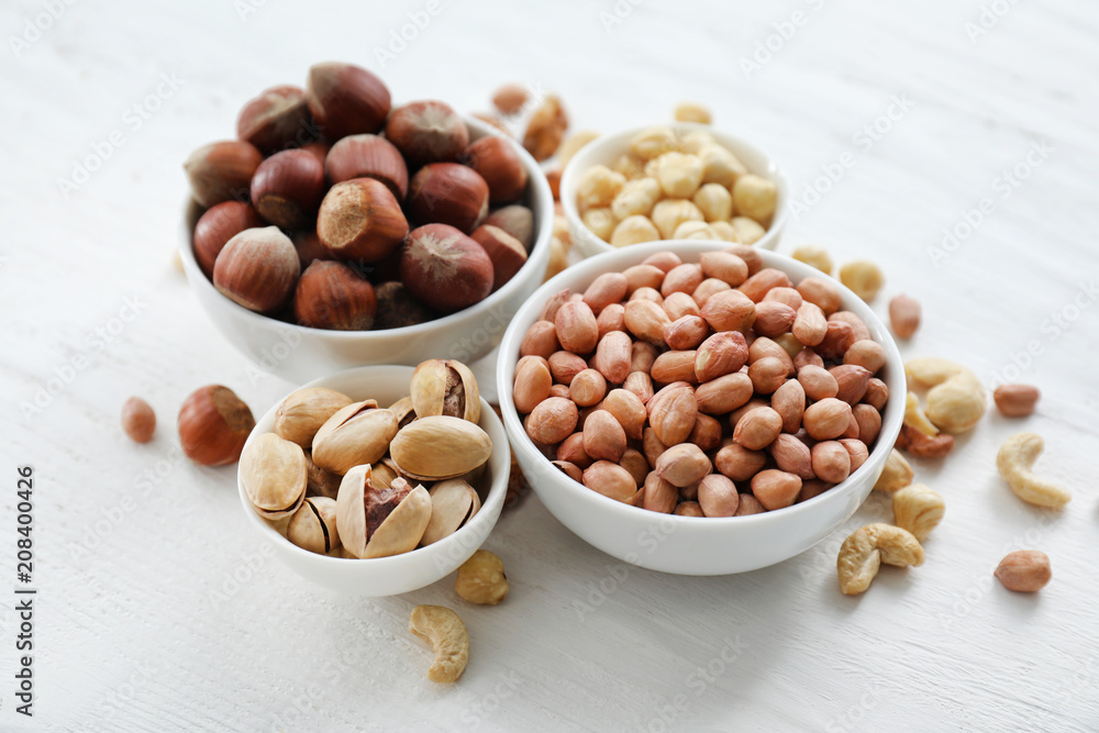 Bowls with different kinds of nuts on light background