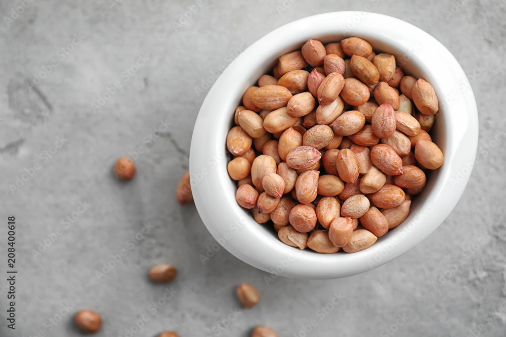 Bowl with peanuts on grey background, top view