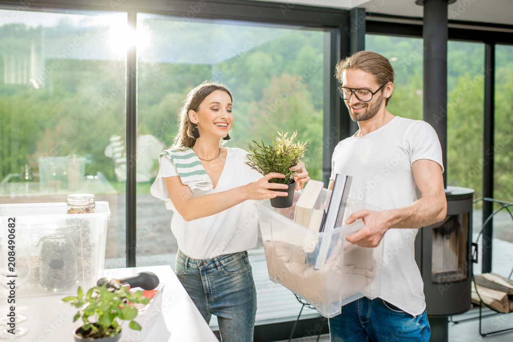 Young and happy couple unpacking different home stuff making order in their new and modern house