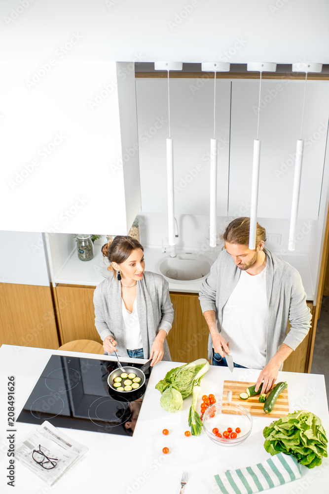 一对年轻快乐的夫妇穿着灰色毛衣，在现代厨房里烹饪蔬菜