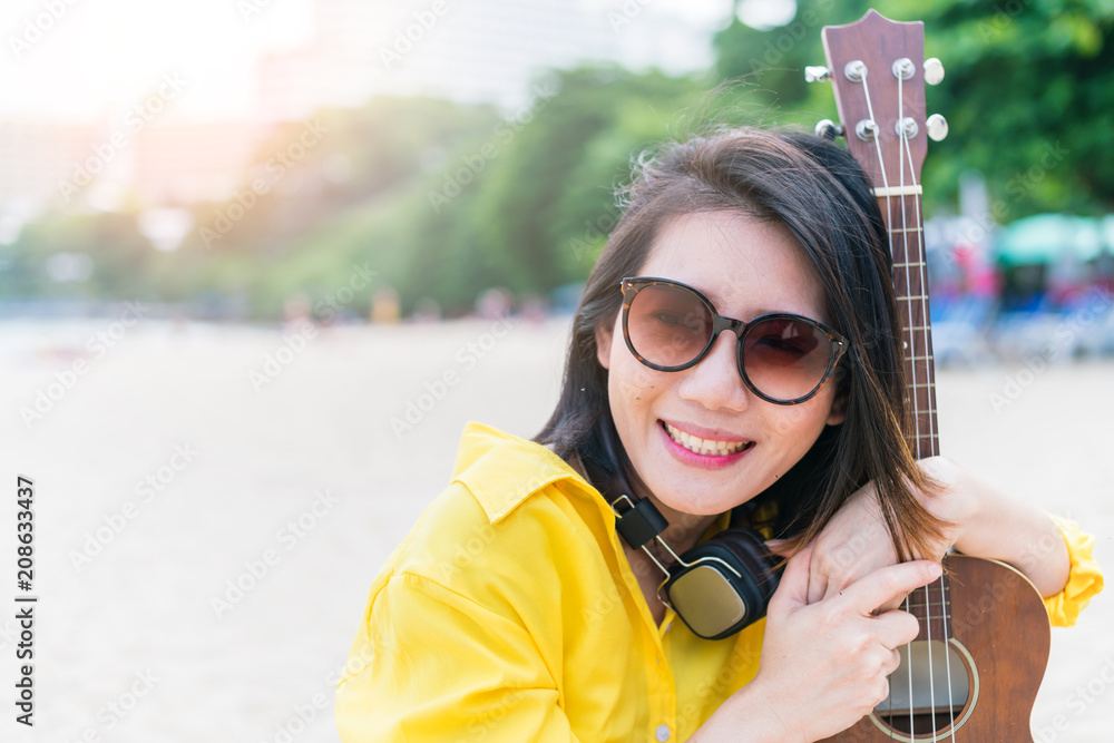 美丽的亚洲女人在芭堤雅海滩用尤克里里琴享受假期