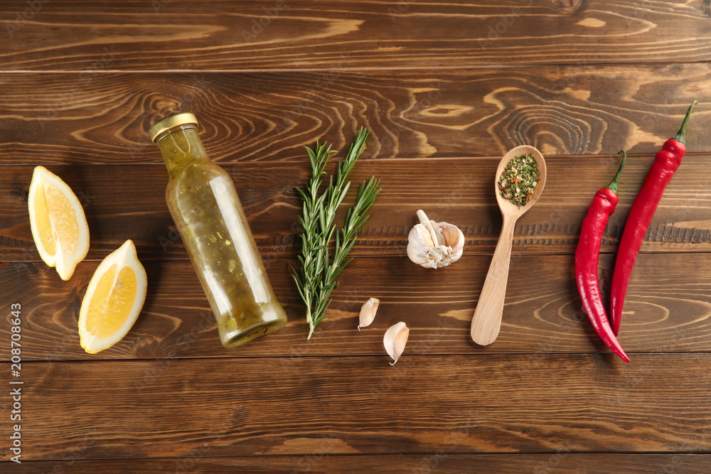 Composition with bottle of tasty sauce and condiments on wooden background, flat lay