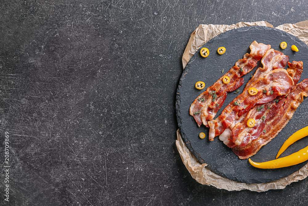 Slate plate with tasty fried bacon on dark background