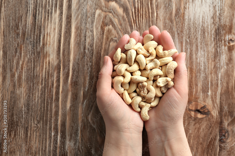 Female hands with tasty cashew nuts on wooden background