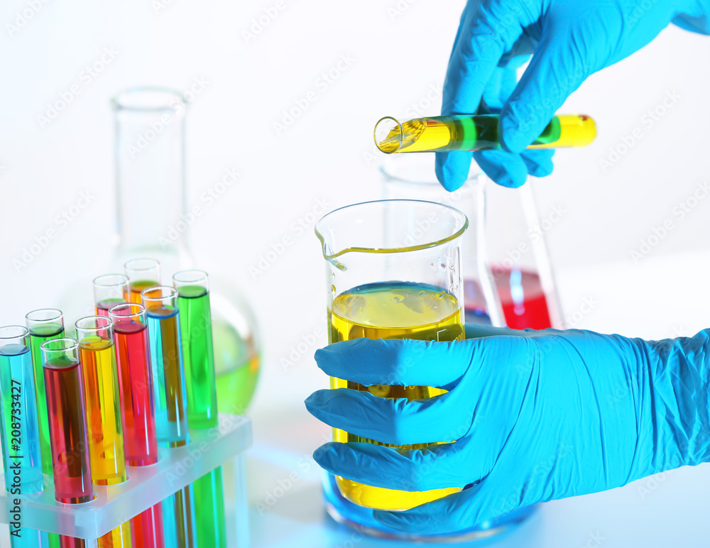 Laboratory worker pouring liquid from test tube into beaker on light background, closeup