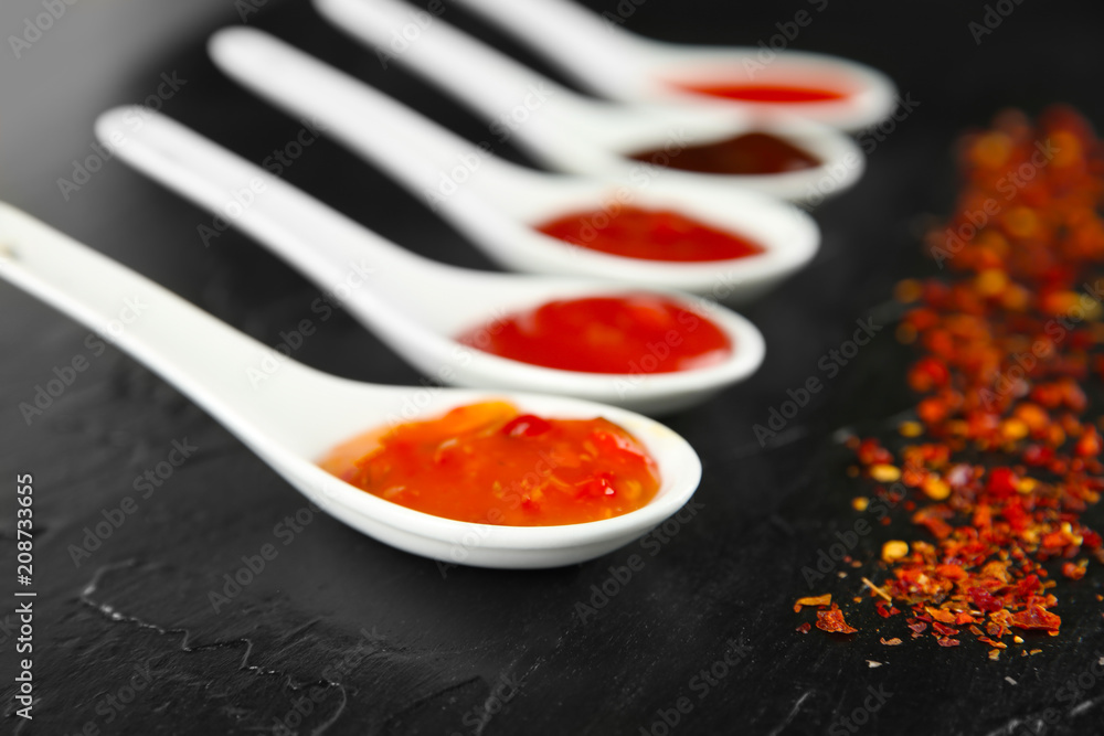 Spoons with red sauces on black background