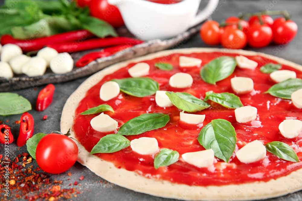 Raw dough for pizza with red sauce and ingredients on table