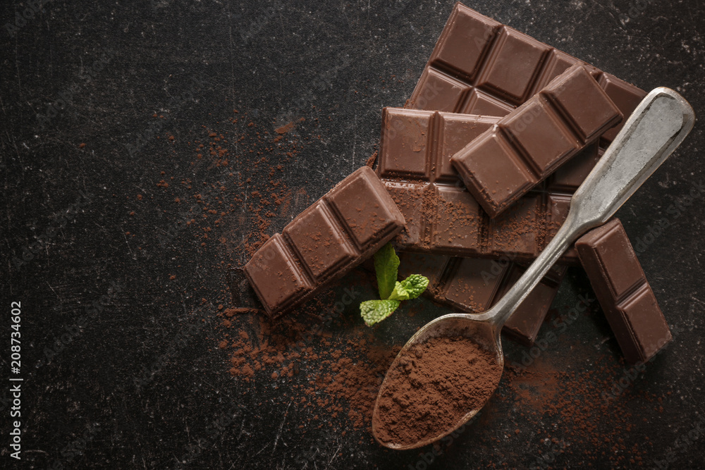 Spoon with cocoa powder and tasty chocolate on dark background, top view