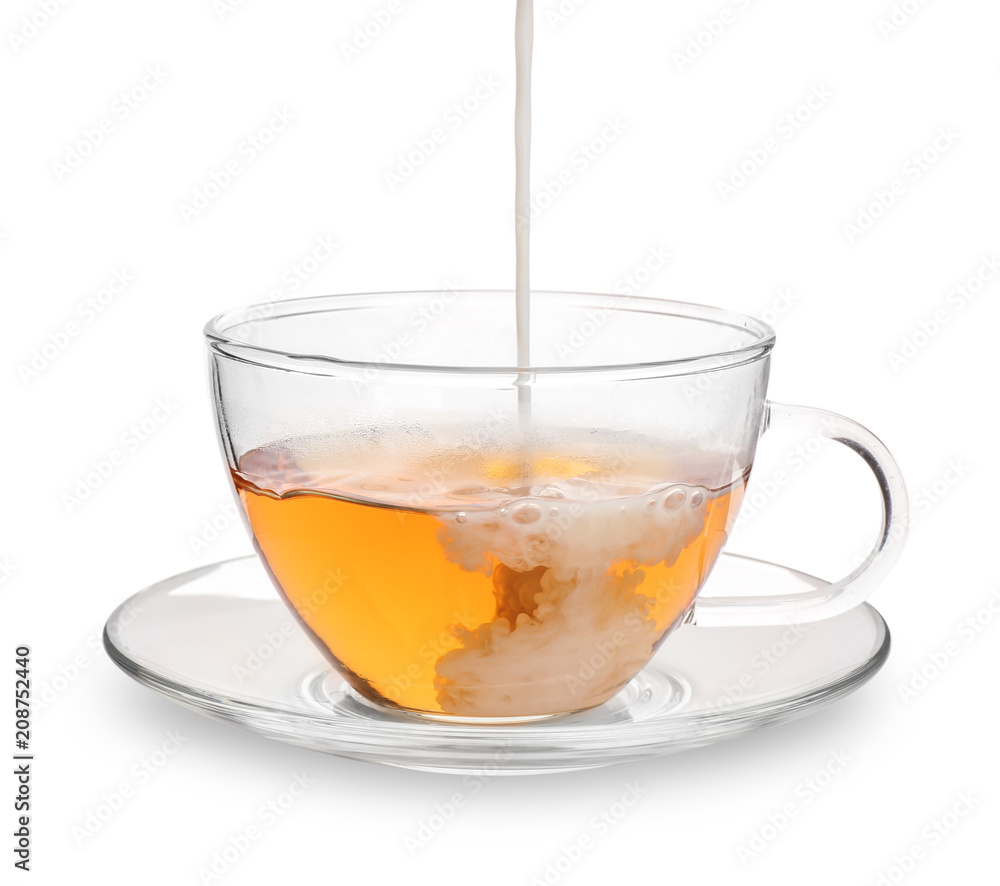 Pouring milk into glass cup with aromatic tea on white background