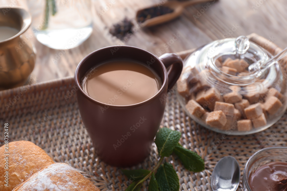 Cup of aromatic tea with milk on wicker tray