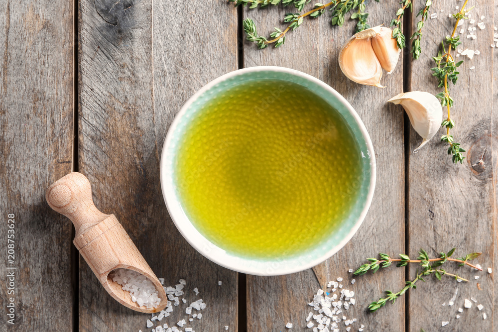 Bowl of olive oil, garlic and scoop with salt on wooden background, top view