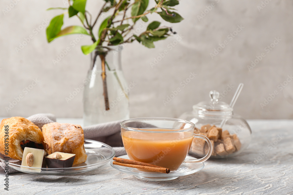 Cup of hot masala tea, cinnamon sticks and treats on wooden table