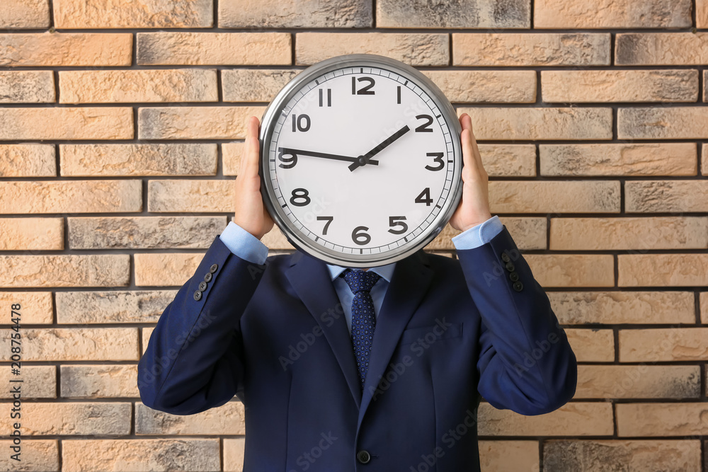 Man holding clock on brick background. Time management concept