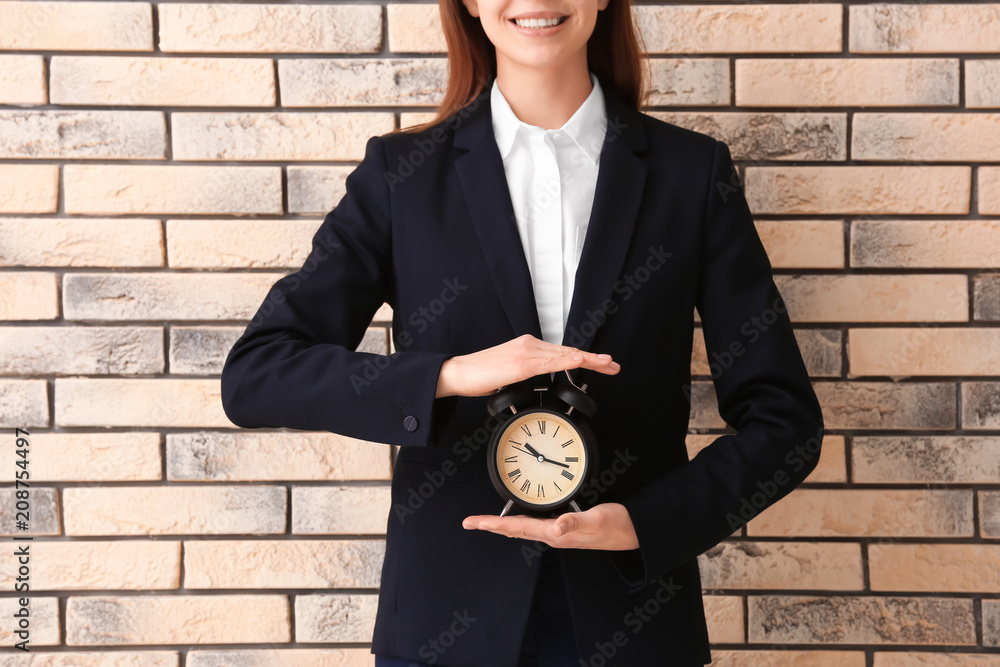 Woman holding alarm clock on brick background. Time management concept