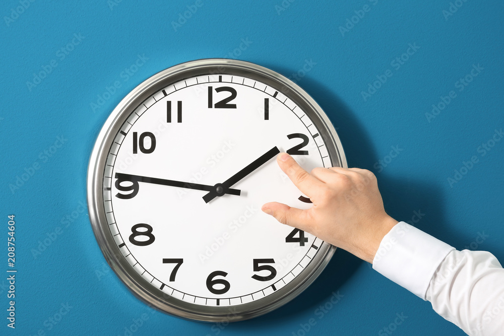 Man pointing on clock against color background. Time management concept