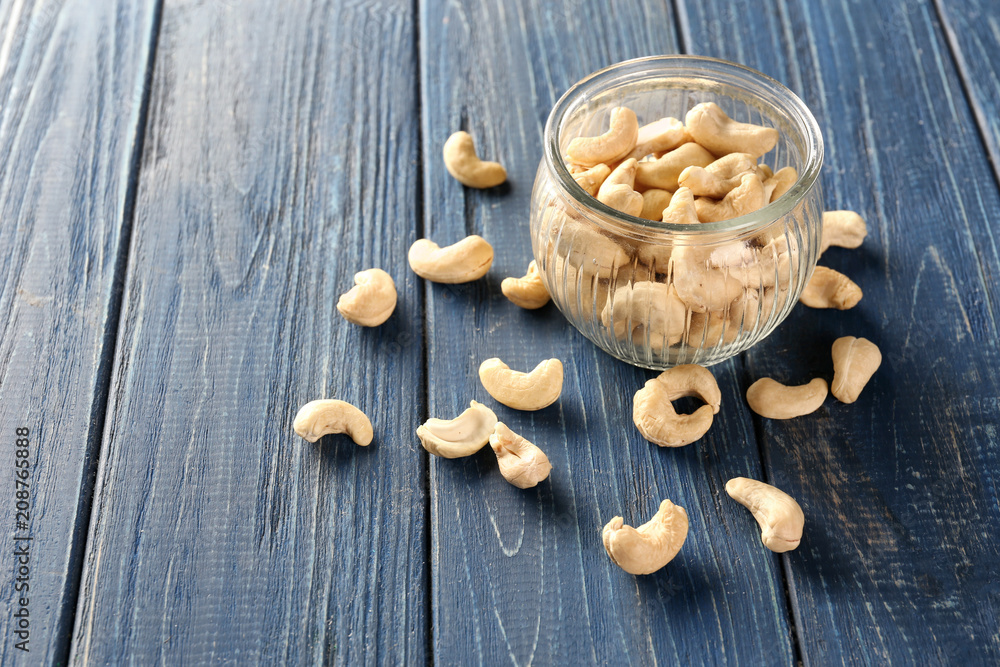 Tasty cashew nuts and glass jar on wooden background