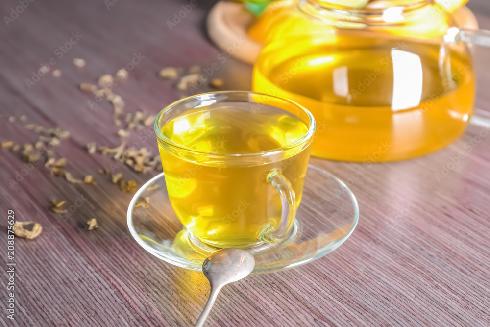 Delicious green tea in glass cup and pot on wooden background