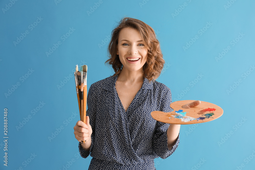 Female artist with brushes and paint palette on color background