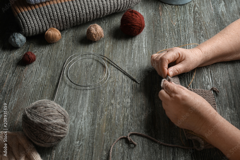 Senior woman knitting sweater at table