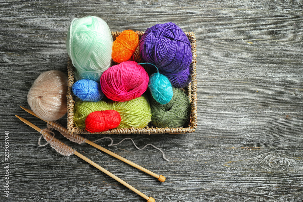 Wicker basket with knitting yarn and needles on wooden table