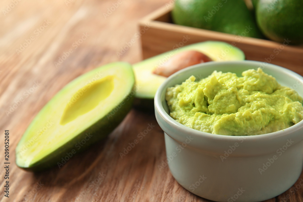 Bowl with tasty guacamole and ripe avocados on wooden table