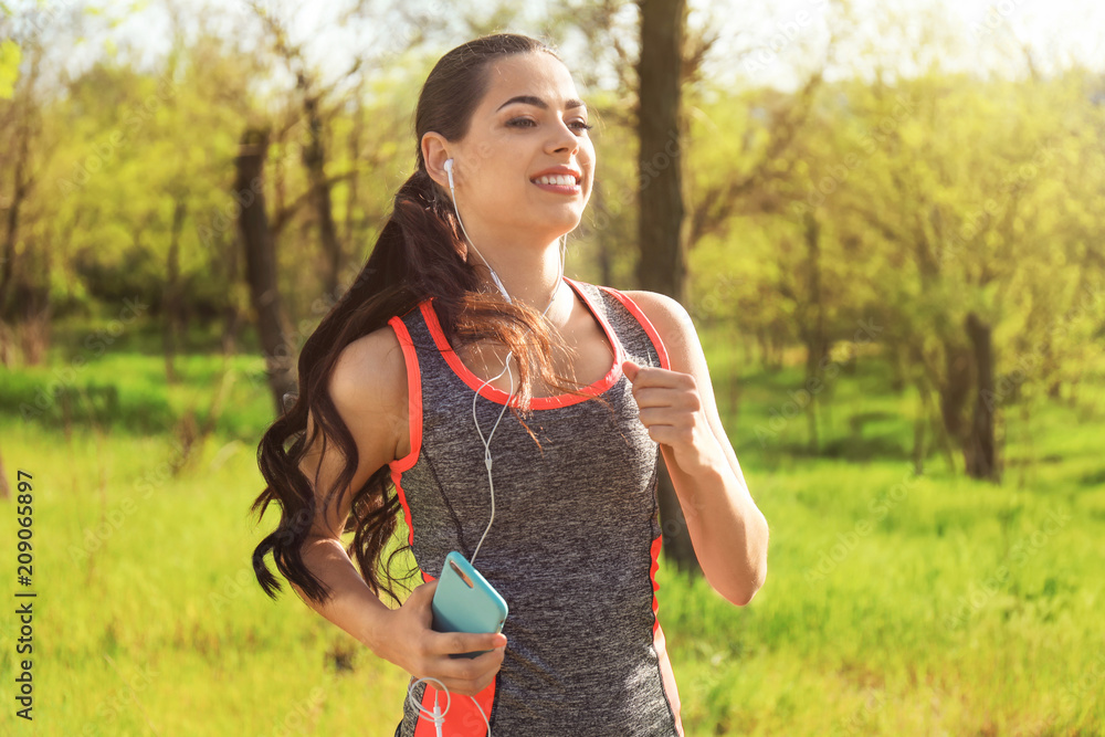 Sporty young woman listening to music while running in park