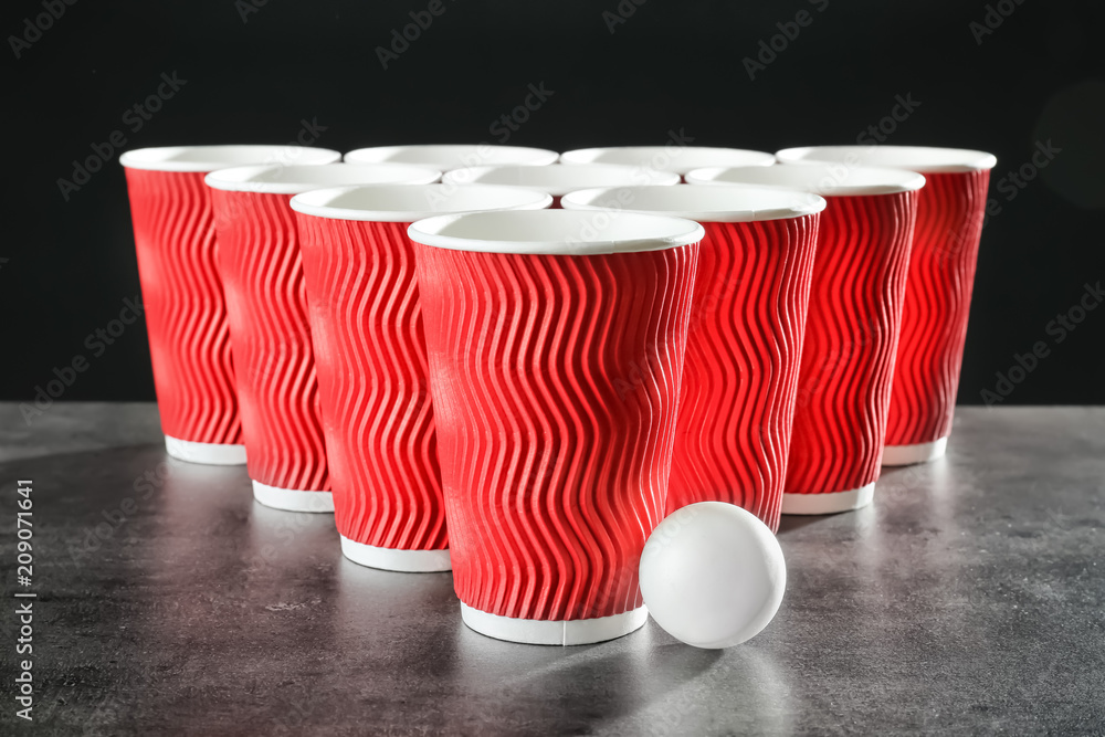 Cups and ball for beer pong on table against dark background