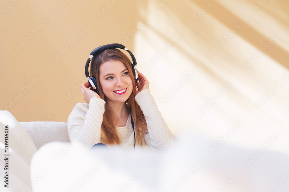 Happy young woman listening to music on headphones at home